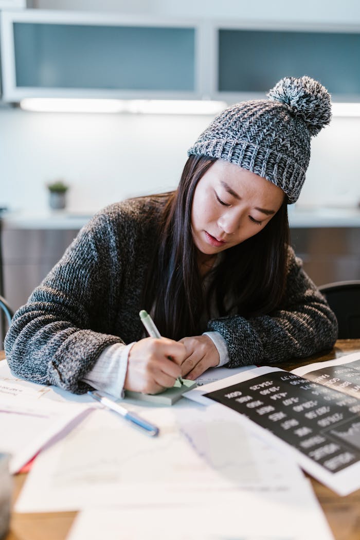 Focused young entrepreneur writing business notes in a cozy indoor setting wearing a warm beanie.